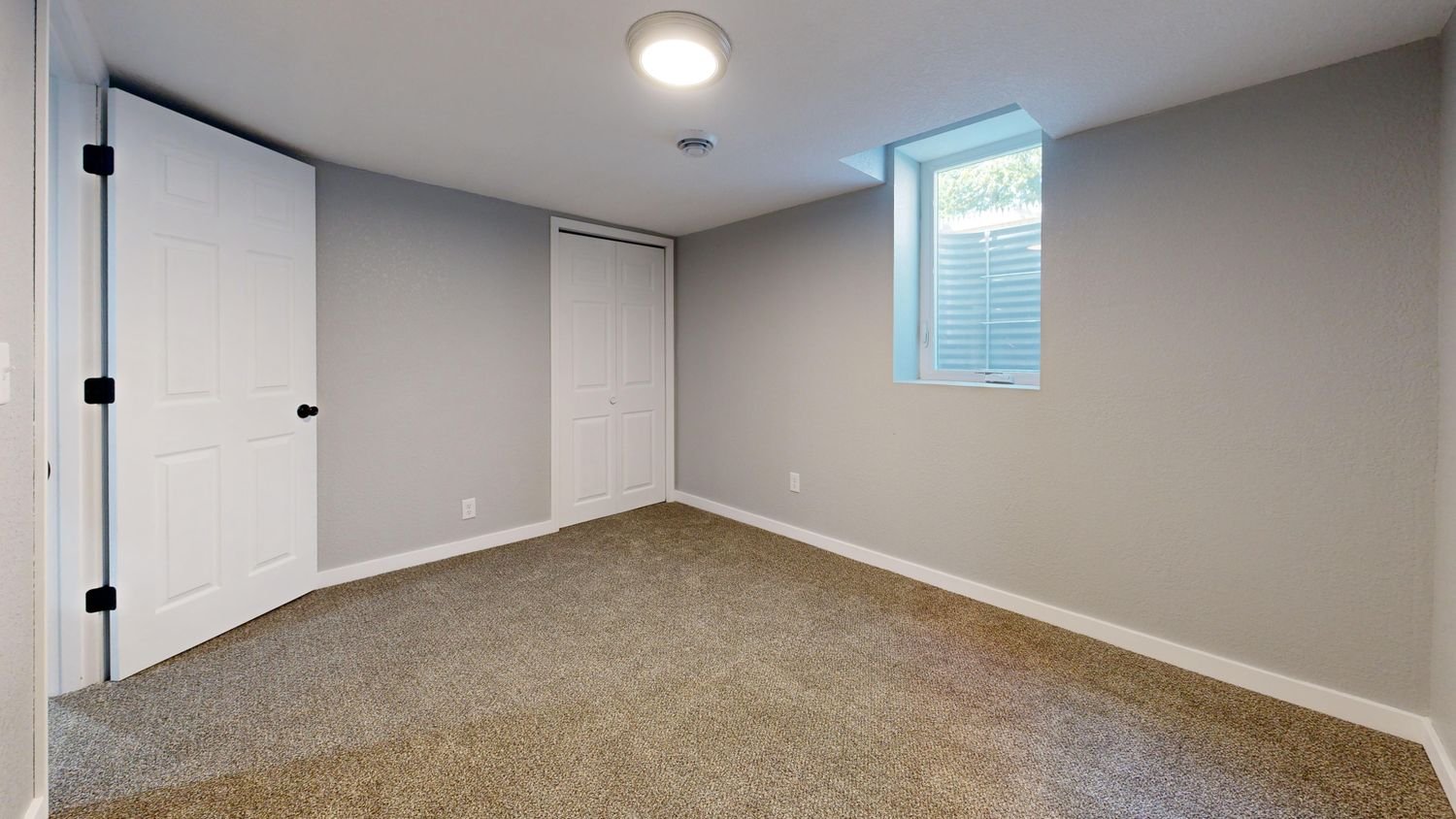 Basement room with new carpet, white doors and a daylight window