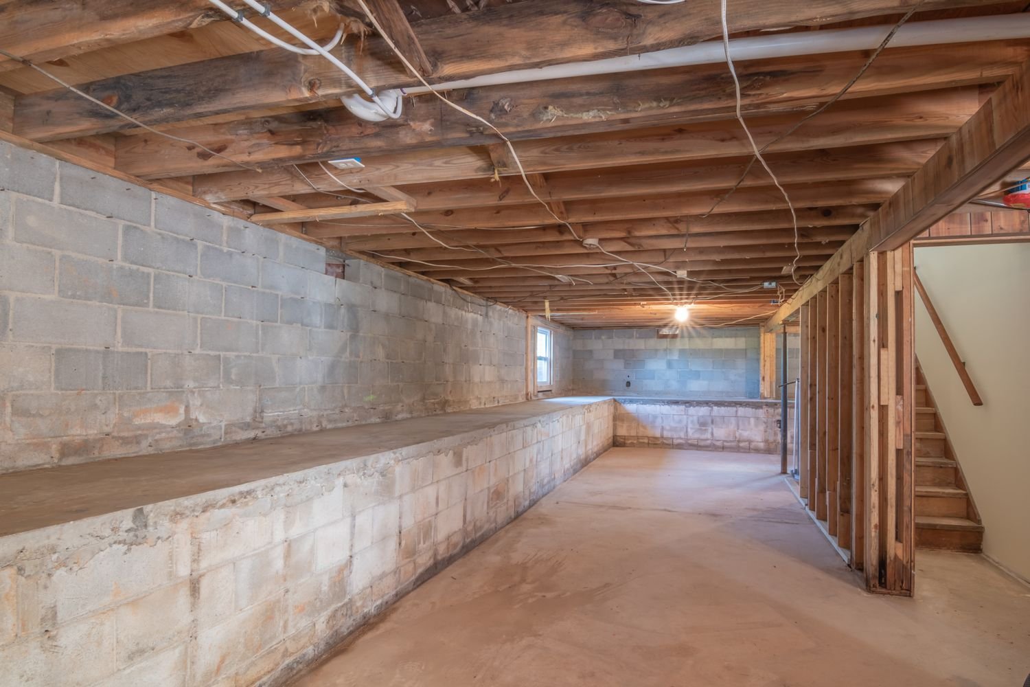 Unfinished basement with exposed floor joists and concrete walls